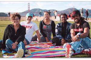 Five people sit on a colorful, striped blanket at Presidio Tunnel Tops