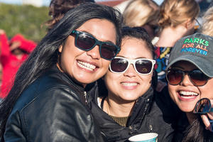Three woman wearing sunglasses smile for photo.