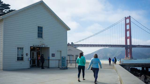 Two women walking down paved path towards the Golden Gate Bridge.