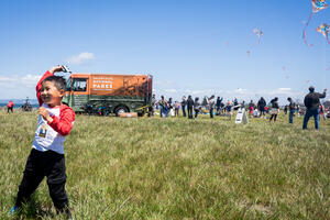 A child smiles flying a kite alongside the Roving Ranger at Crissy Field.