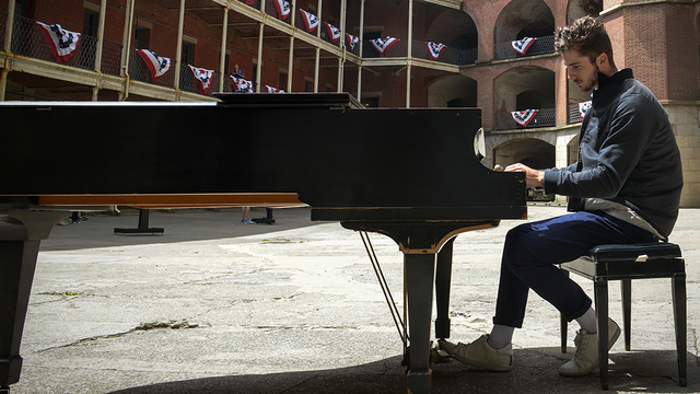 Pianist plays piano surrounded by the red-bricked Fort Point.