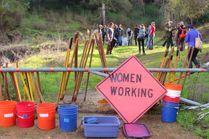 Sign saying "Women Working" with a trail crew in the background.