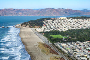 Aerial view of Ocean Beach showing waves lapping against the shore before San Francisco, along with the Golden Gate and Marin Headlands in the background.