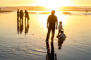 Visitors and families bask in a golden sunset where the water meets the sands of Ocean Beach.