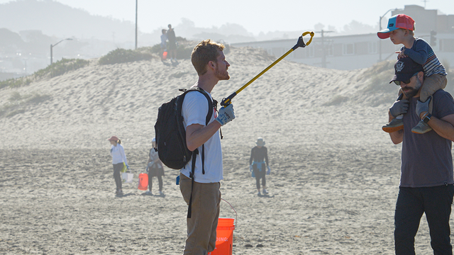 Adult shows trash to curious boy on his dad's shoulders on Ocean Beach in San Francisco.