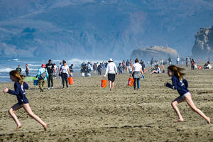 Two girls run in foreground of a wide shot of a crowded Ocean Beach.