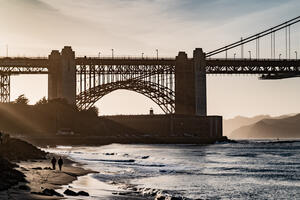 Sunlight filters through the silhouetted Fort Point and Golden Gate Bridge