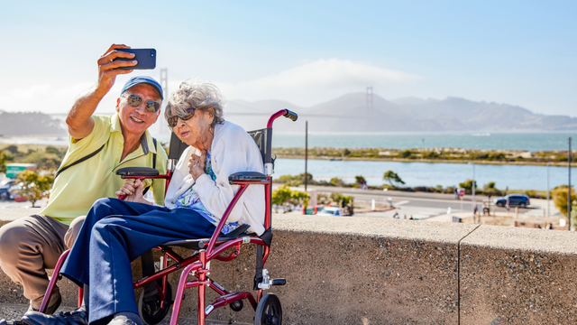 Elderly couple poses for a selfie before the Golden Gate Bridge at Presidio Tunnel Tops.