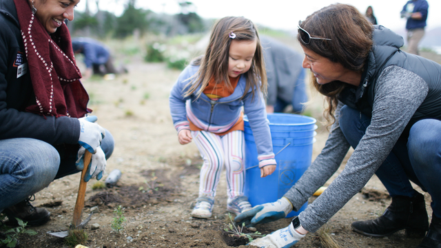 Parks Conservancy staff and volunteers smiling as they plant saplings in the parks.