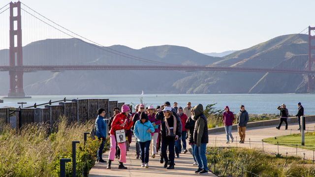 A group of event participants on a walking tour of the Presidio Tunnel Tops. Golden Gate Bridge and Marin Headlands are seen in the background.