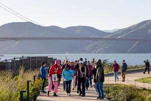A group of event participants on a walking tour of the Presidio Tunnel Tops. Golden Gate Bridge and Marin Headlands are seen in the background.