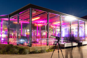 Long exposure photo of an enclosed outdoor picnic area in the Presidio glows with bright pink lights with an astronomy telescope seen in the foreground