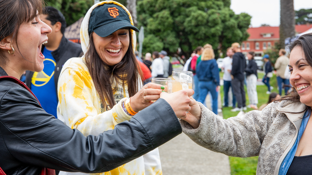 Three smiling and laughing women raise their glasses at the Parks4All: Brewfest in the Presidio