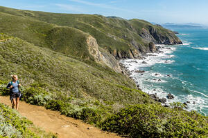 A hiker looks out at scenic view of the pacific coastline from the Coastal Trail in Marin Headlands on a bright sunny day.