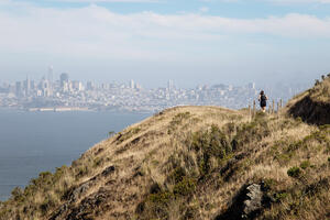 A park visitor runs on the SCA Trail in the Marin Headlands with the San Francisco skyline in background.