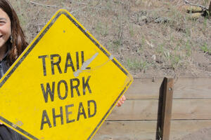 woman holding sign that says "Trail Work Ahead"