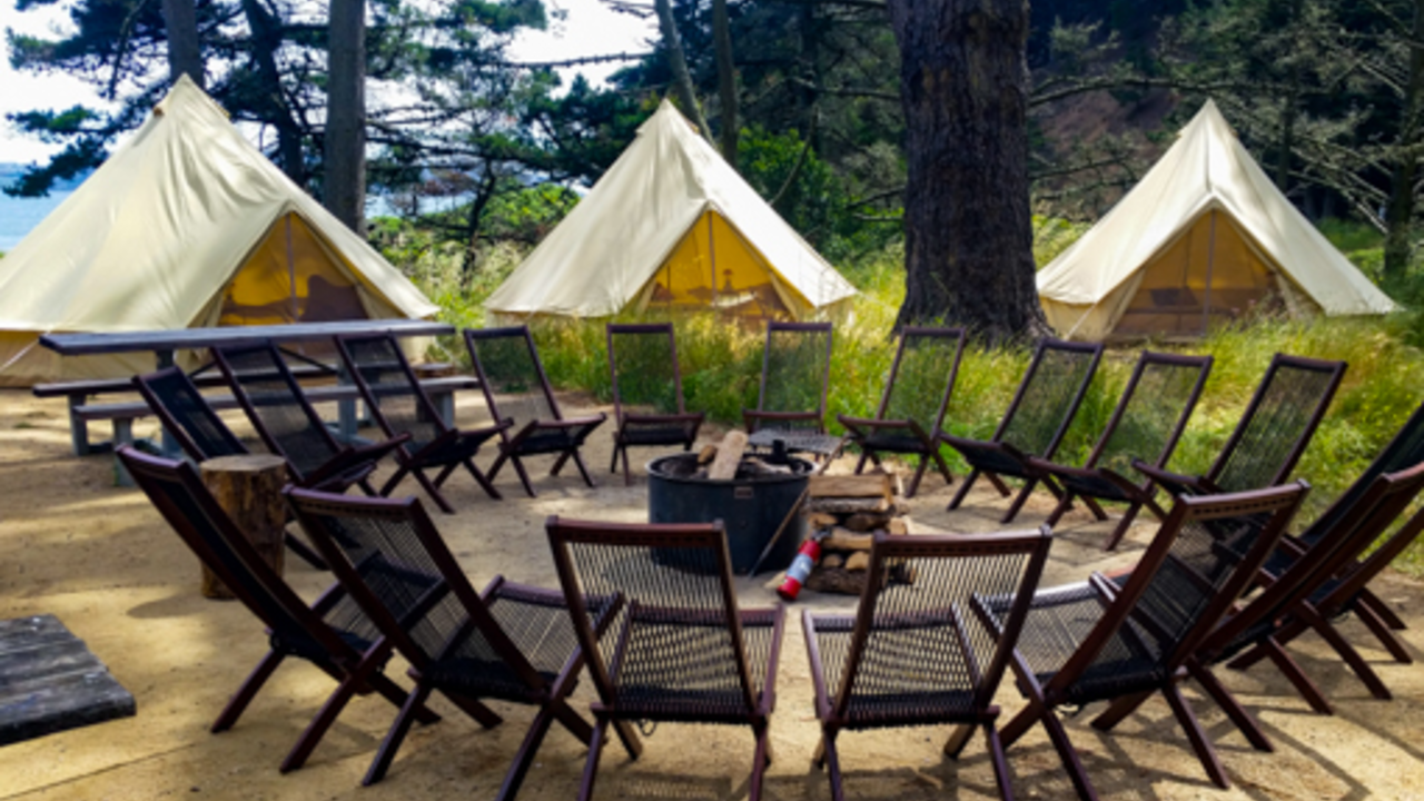 Chairs surround a campfire with tents and trees in the background at Kirby Cove.