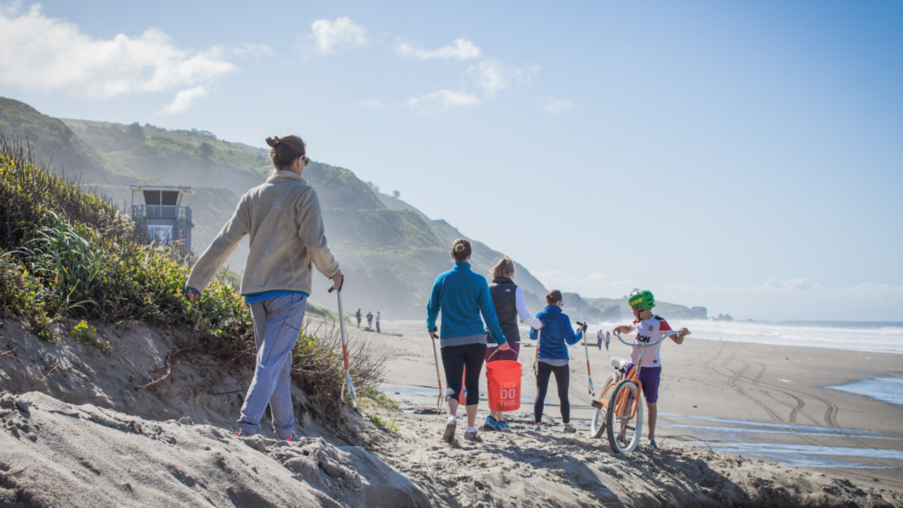 A group of volunteers walk onto Stinson Beach with buckets and grabbers for a day of beach clean-up.