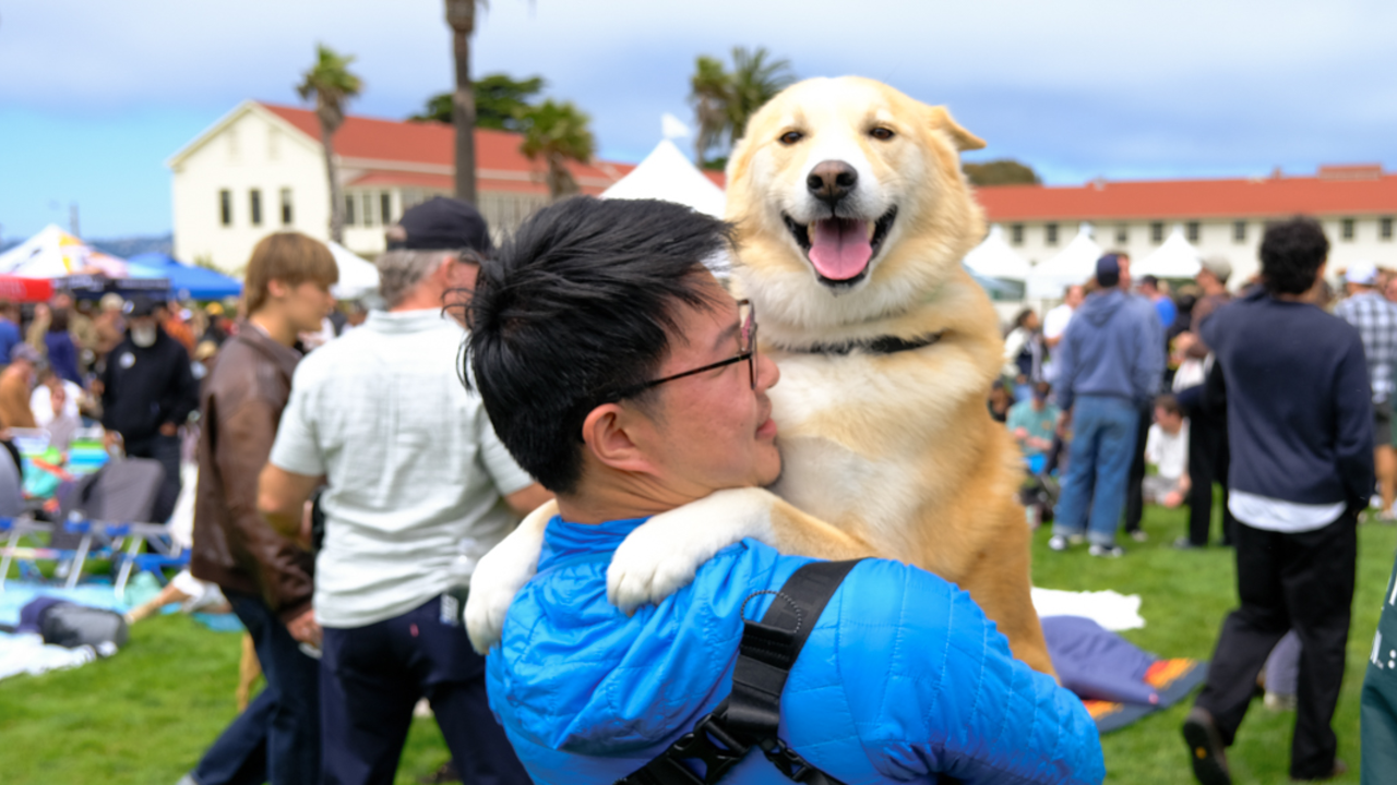 A Parks4All: Brewfest attendee holds his happy dog up in his arms who smiles at the camera in Presidio of San Francisco