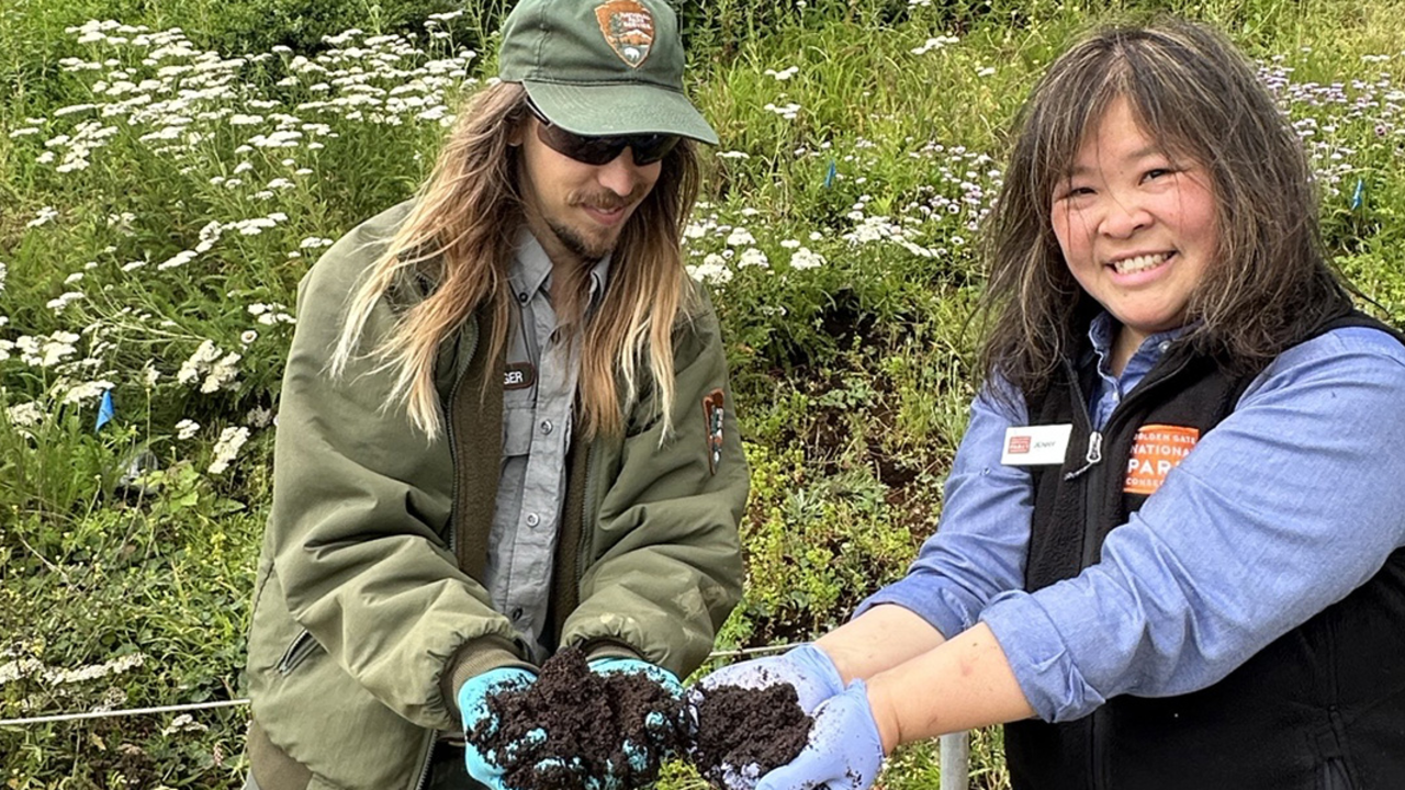 Two people hold up coffee grounds for a park project