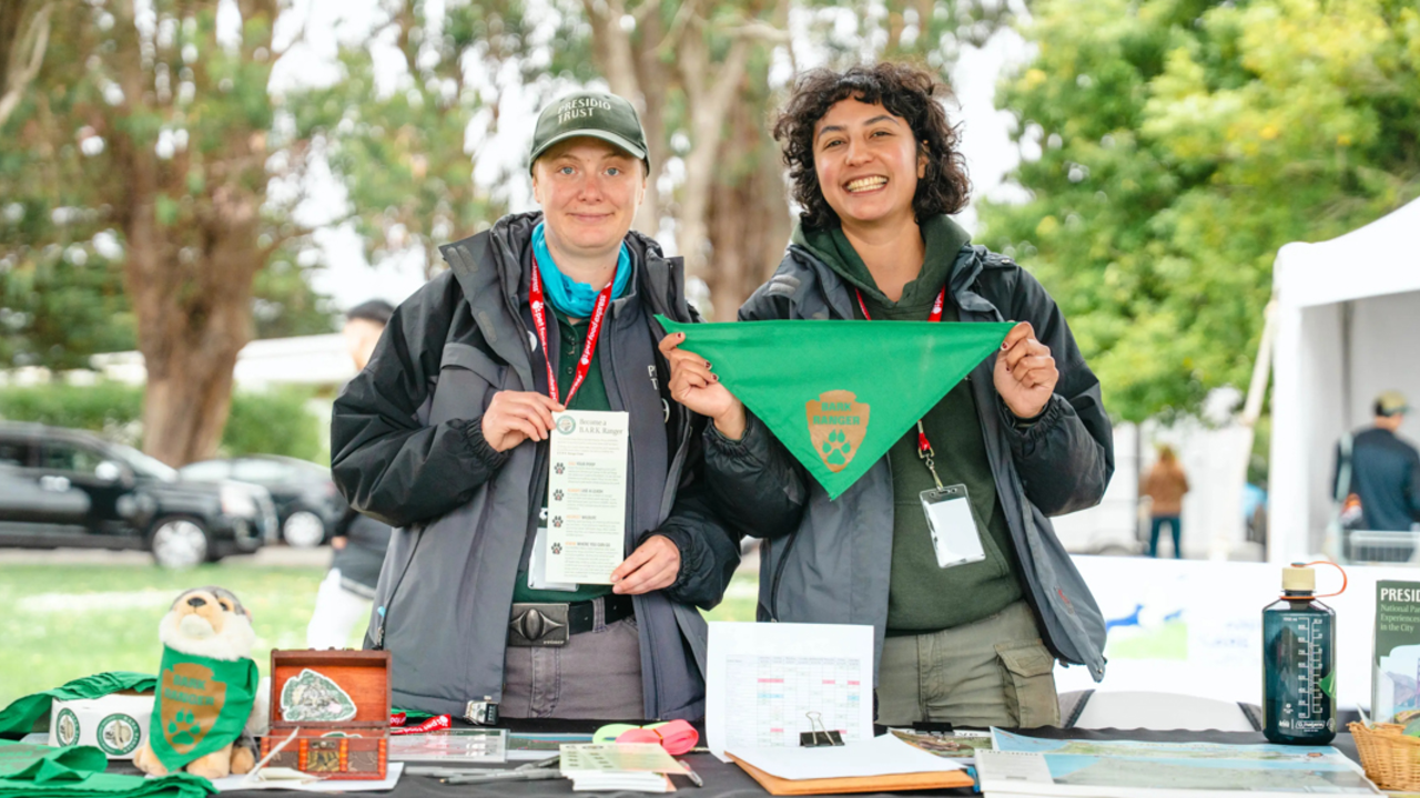 Two Presidio Trust staff members holding a dog bandanna for BARK rangers in the Presidio of San Francisco