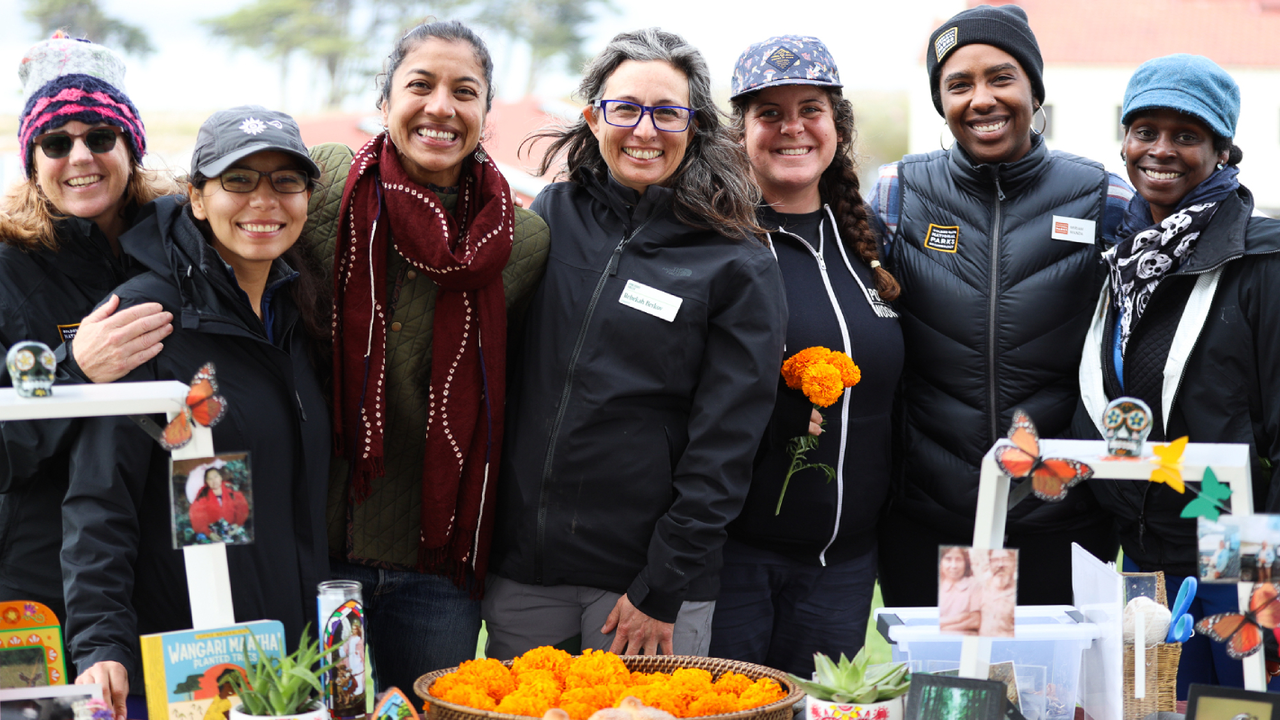 A group of people smile for a photo in font of an Ofrenda to celebrate Dia de los Muertos