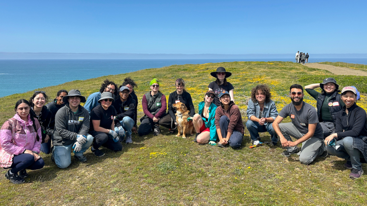 A group of volunteers pose for a group photo during the Belonging in Nature event on a sunny day at Mori Point in the Golden Gate National Recreation Area.