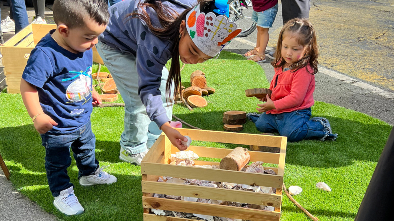 Children play and interact with natural objects on a turf lawn, simulating green space in the San Francisco tenderloin district at the Golden Gate Greenway with the Parks Conservancy Roving Ranger.