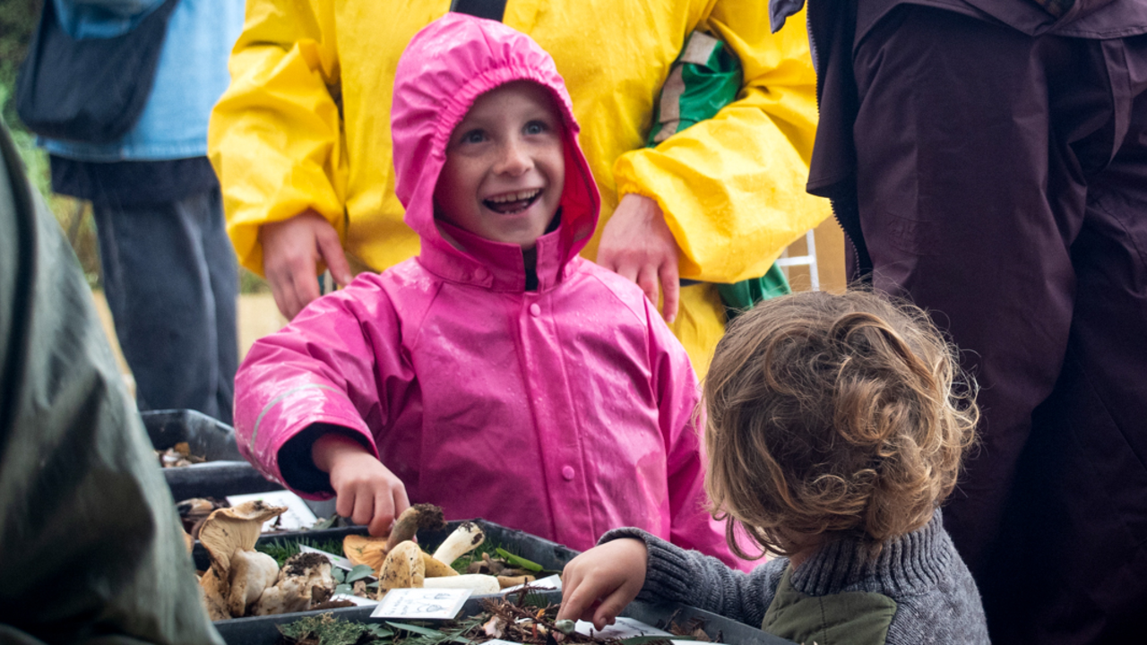 A child smiles gleefully before a table of mushroom specimen at the Fungi Fair in the Presidio of San Francisco
