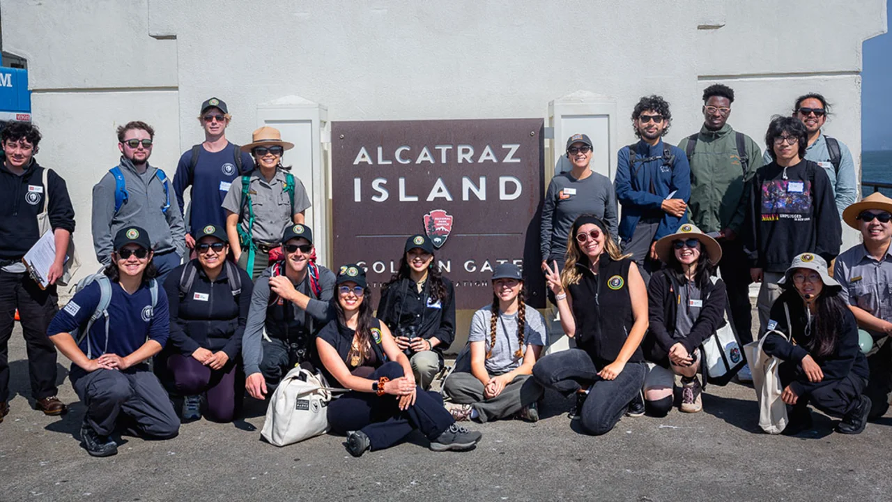 2024 Academic Interns and Conservancy Fellows pose in front of the Alcatraz Island sign after touring the island and stewarding the Alcatraz Garden.
