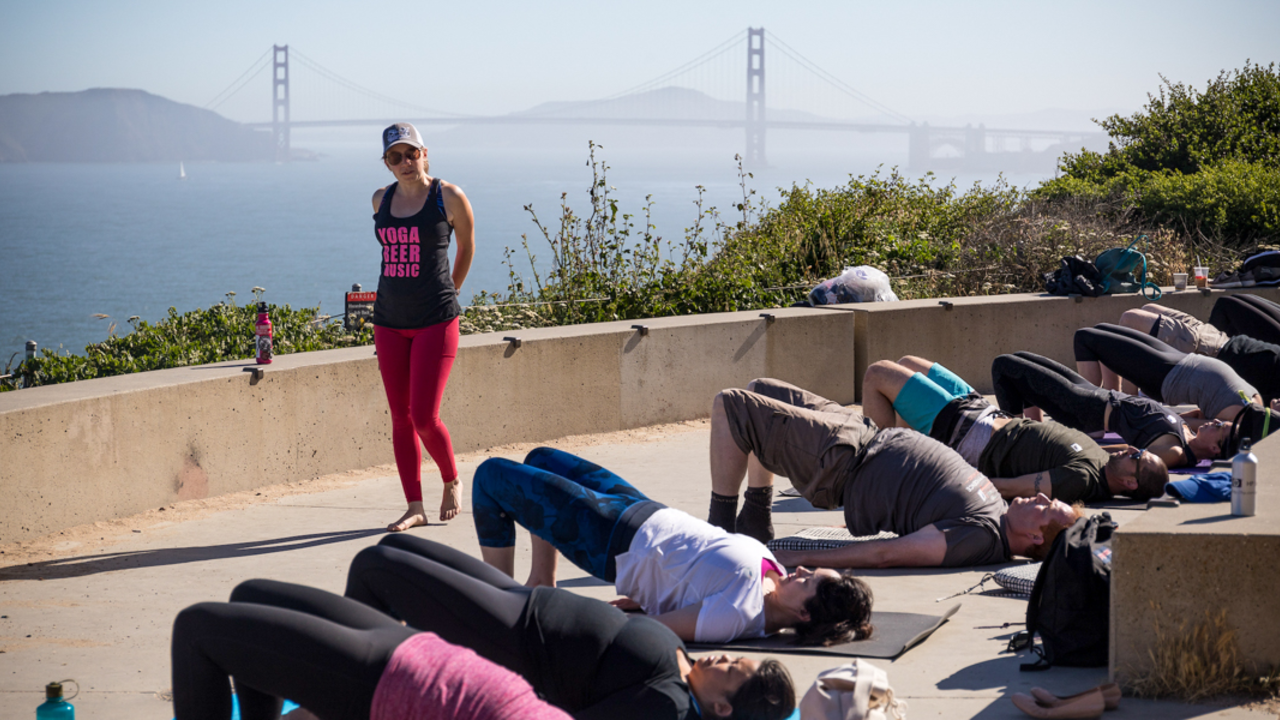 A Yoga instructor leads a group for a healthy day in the parks at Lands End in San Francisco, the Golden Gate Bridge is seen in the sunny background.