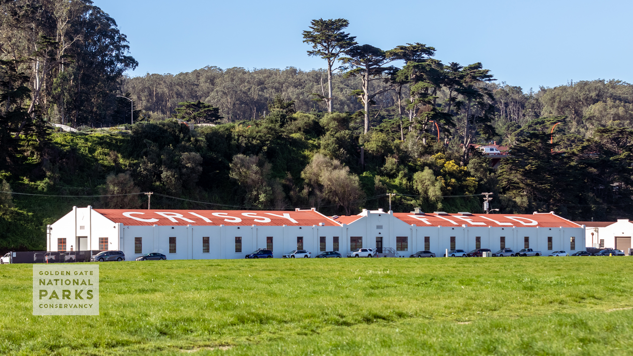 A scenic photo from the lawn of Crissy Field of the hangar building with bold letters painted on the roof spelling out CRISSY FIELD. Photo by Kelly Sullivan.