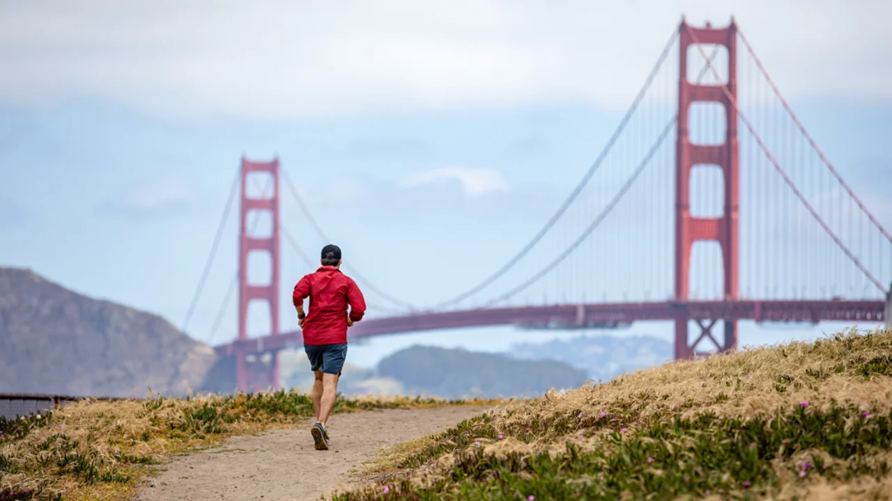 A hiker jogs up a path in the coastal bluffs of Baker Beach in San Francisco with the Golden Gate Bridge seen in the background.