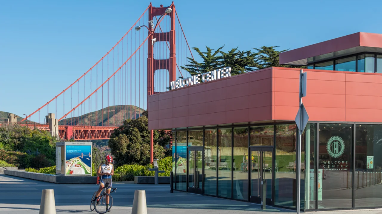 A cyclist on his bike takes a break at the Golden Gate Bridge plaza. You can see the Golden Gate Bridge Welcome Center and the bridge itself in the background.
