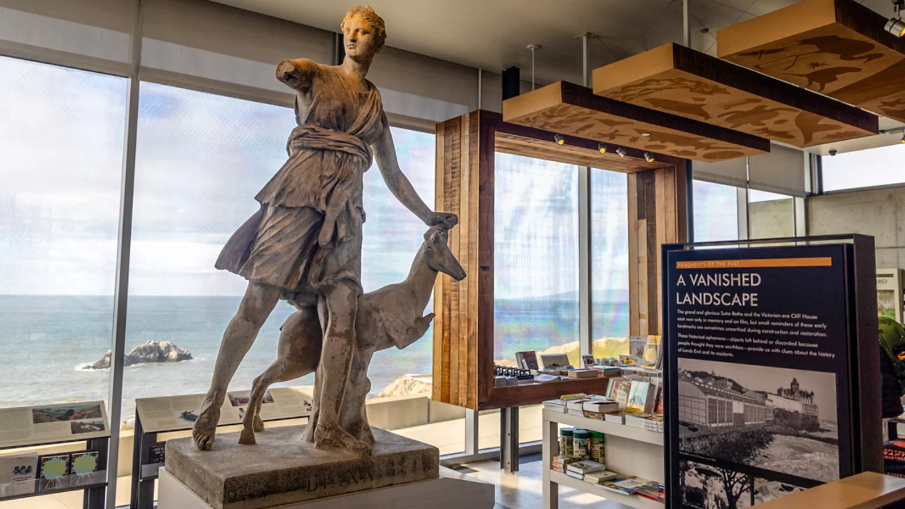 A view from inside the Lands End Lookout, showing a large stone sculpture of Diana, various signs and products, and a view of the pacific ocean through the windows.
