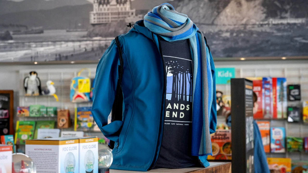 A photo of a merchandise display in the Lands End Lookout showing a sweatshirt, t-shirt, and scarf on a mannequin, various fog globes (snow globes) and other merchandise in the background. 