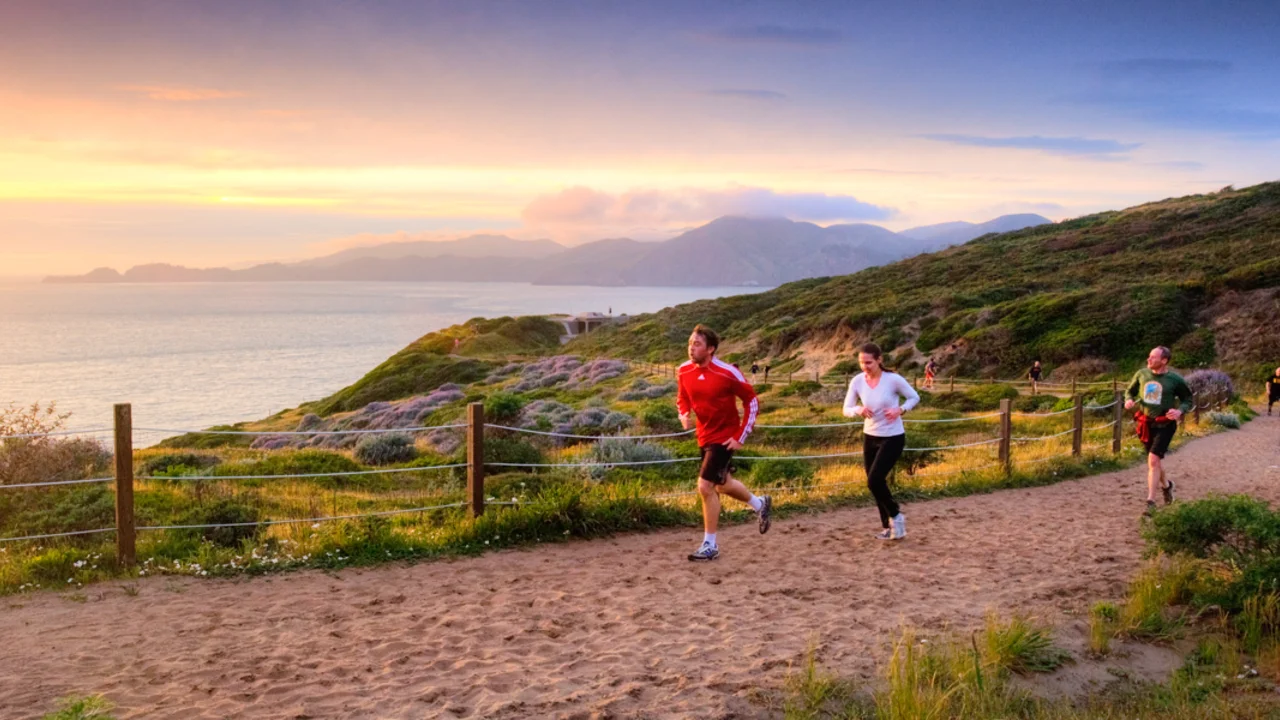 Runners take a coastal trail in the Presidio of San Francisco. Beautiful coastline and pacific ocean view in the background.