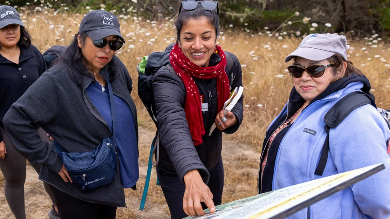 Two Golden Gate National Parks Conservancy community engagement staff members presenting an infographic sign to local community group visitors of Rancho Corral de Tierra.