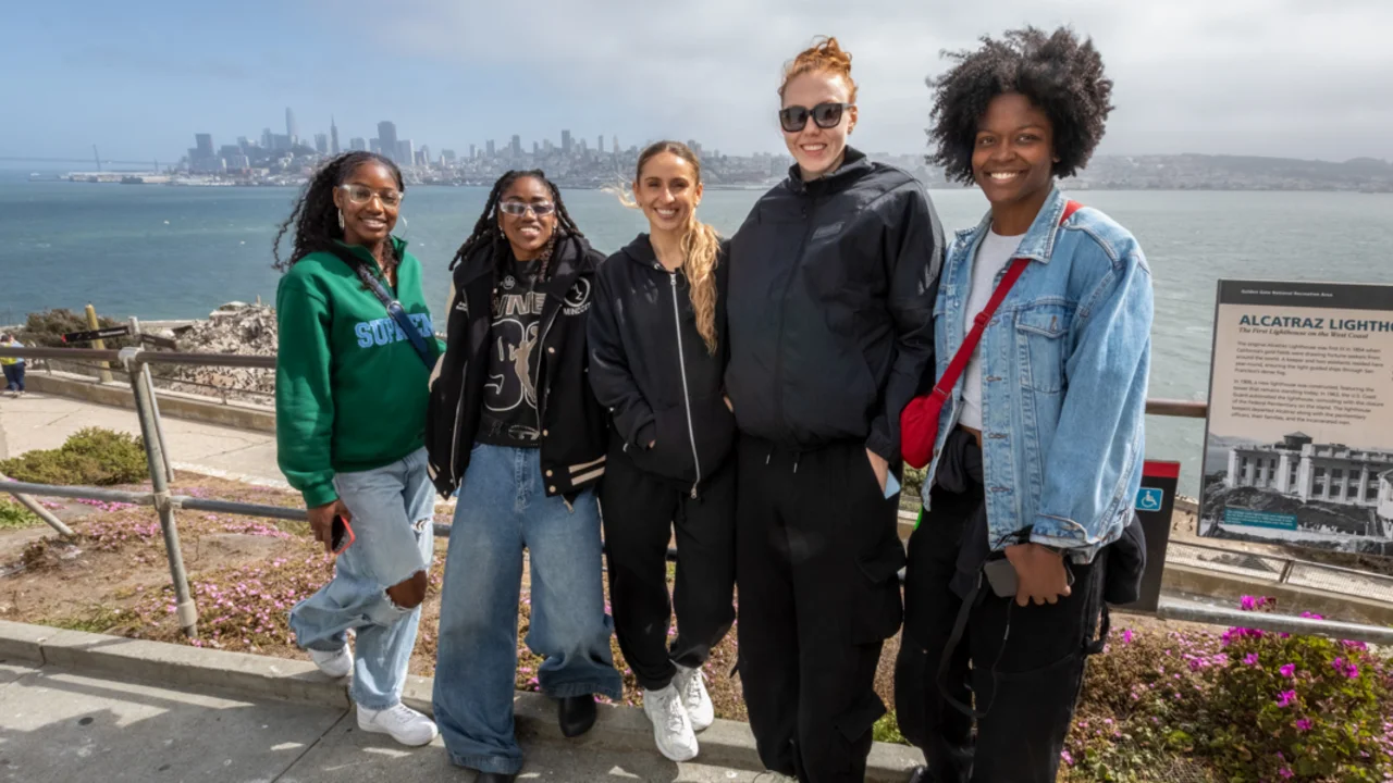 Five individuals pose together on a paved path near Alcatraz Lighthouse, with the San Francisco skyline visible across the bay.