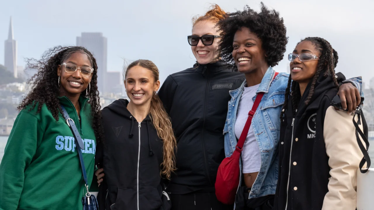 Five young people smile together on a boat with a San Francisco city skyline in the background.