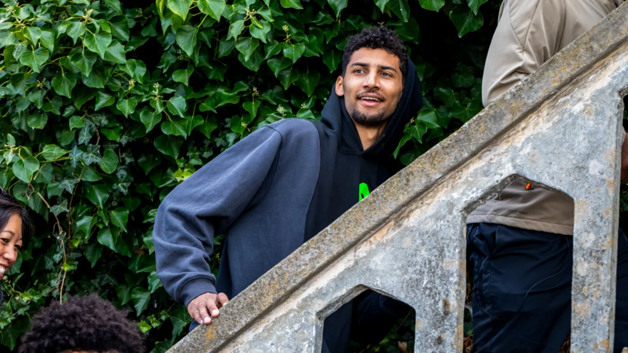 A group of players from the NBA's Golden State Warriors, including one smiling individual in a hoodie, ascend a stairway with a stone railing, lush green ivy behind them.