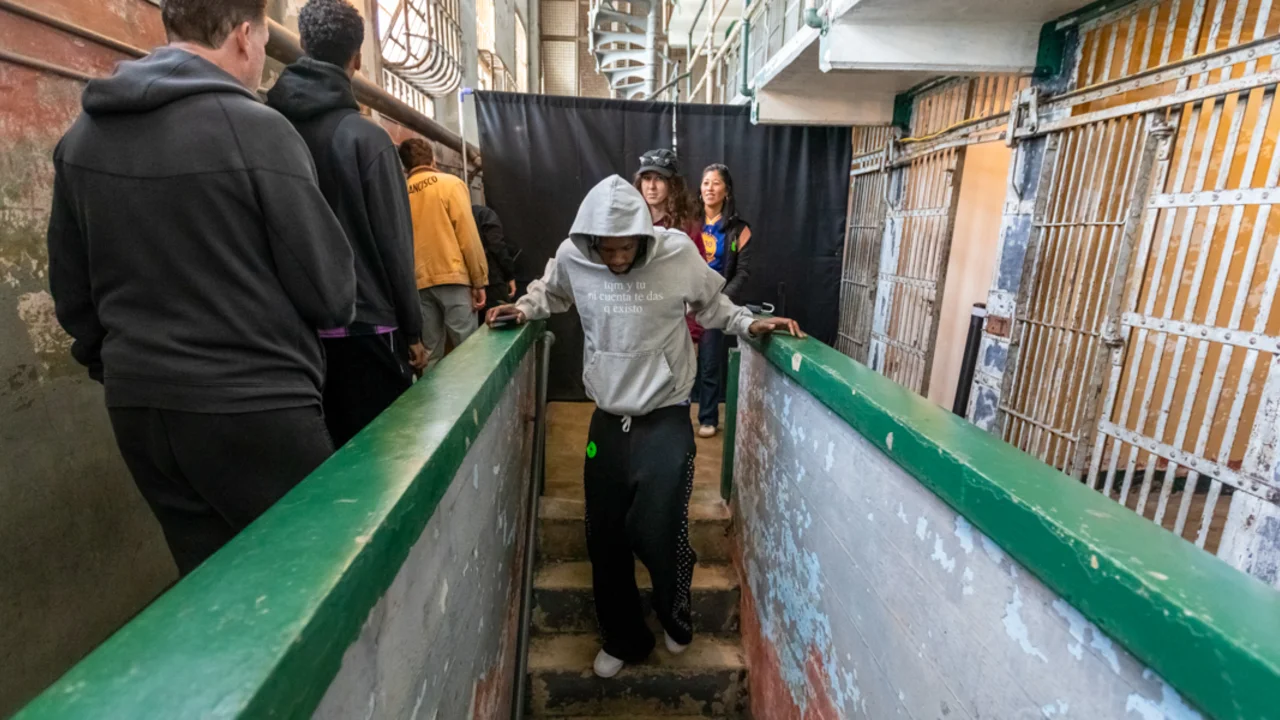 Players from the Golden State Warriors navigate a narrow staircase inside an old prison, with barred cells visible on either side.
