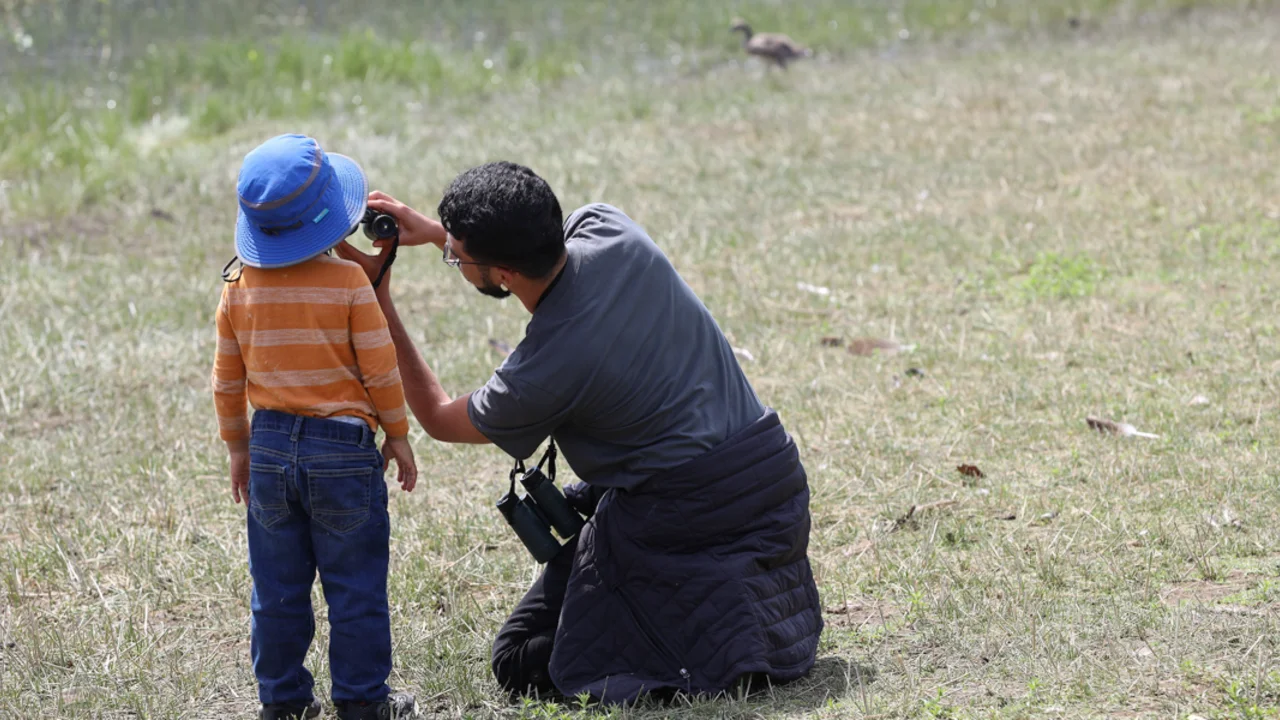 Christian Trujillo and a young participant look through binoculars at a bilingual birding event.