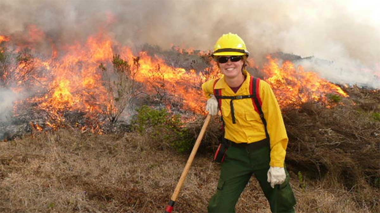 Alison on the scene of a prescribed burn as a fire ecologist. Alison Forrestel poses next to a grassland fire.