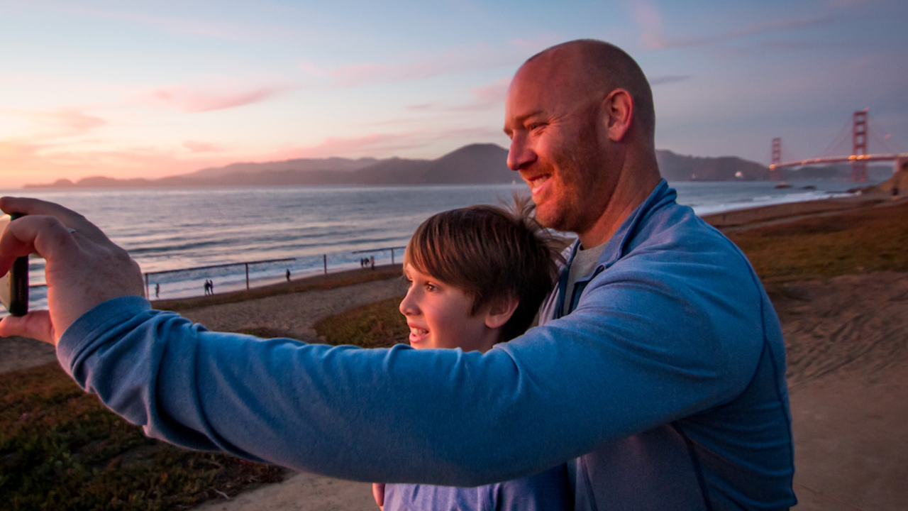 Father and son pose for a selfie at Baker Beach in San Francisco.