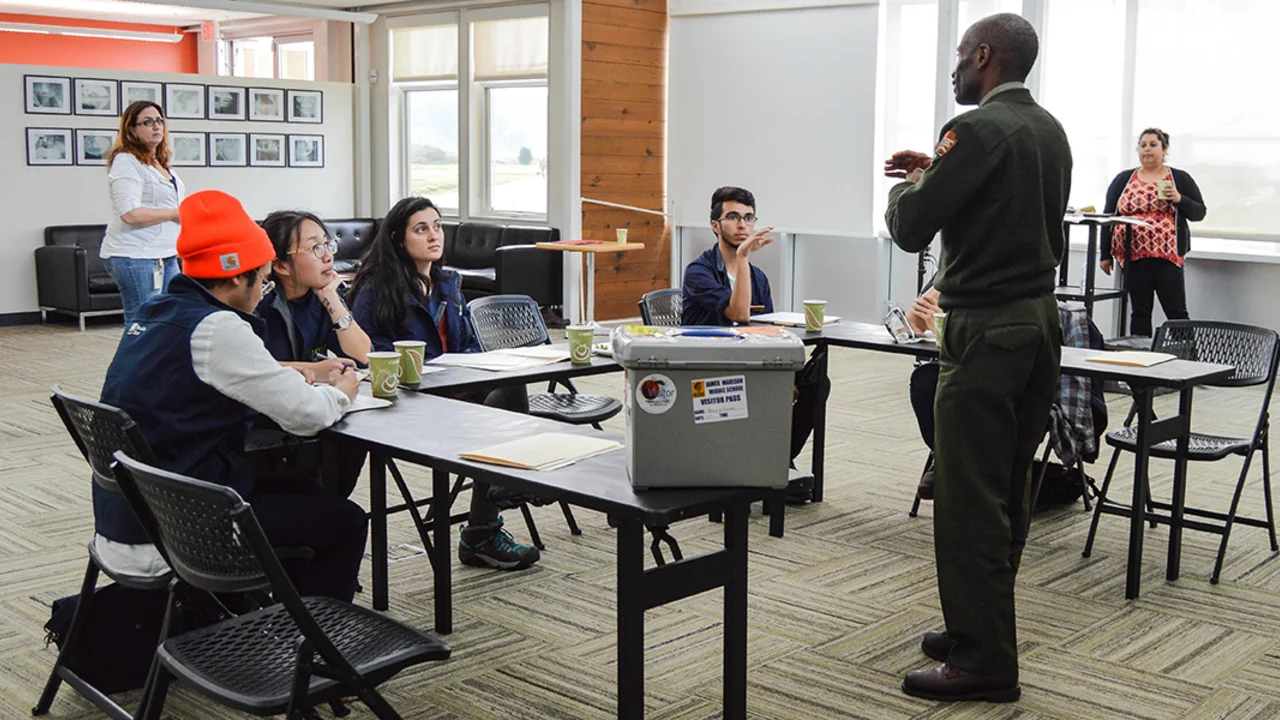 Educators in a classroom sit and listen to a National Park Service Ranger lecturing about educational techniques
