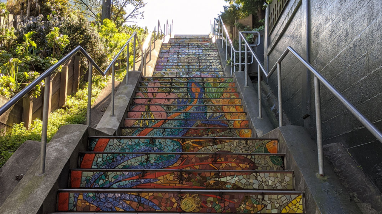 outdoor stairs adorned with colorful tiles are surrounded by plants and trees