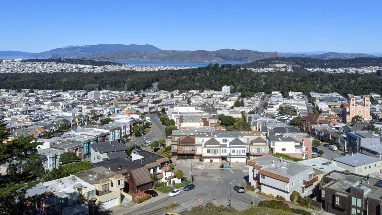 Buildings and cars next to a body of water with rolling hills in the distance