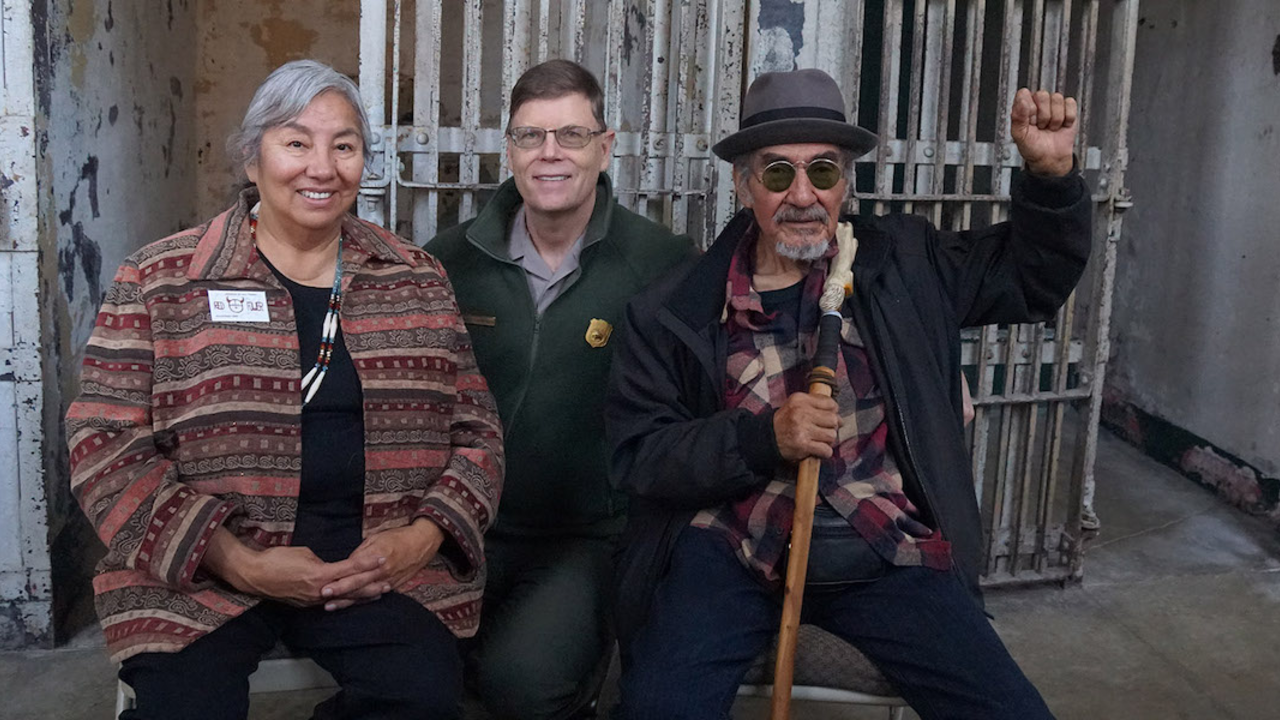 Three people sit smiling for the camera in the Alcatraz Cellhouse