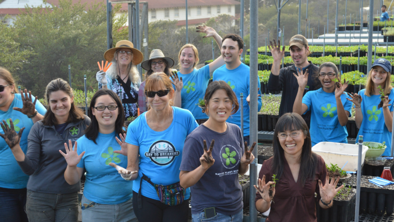 A large group smiles and holds up dirty hand while working in the nursery.